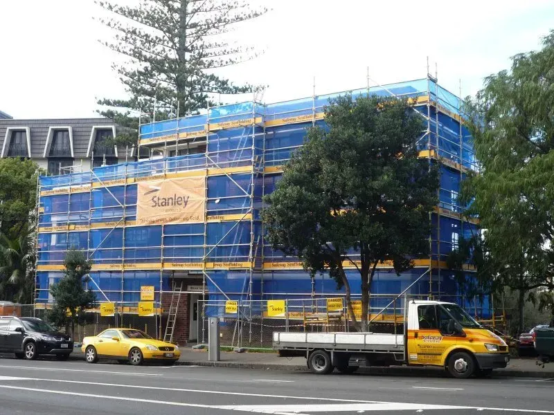 A yellow truck is parked in front of a building under construction
