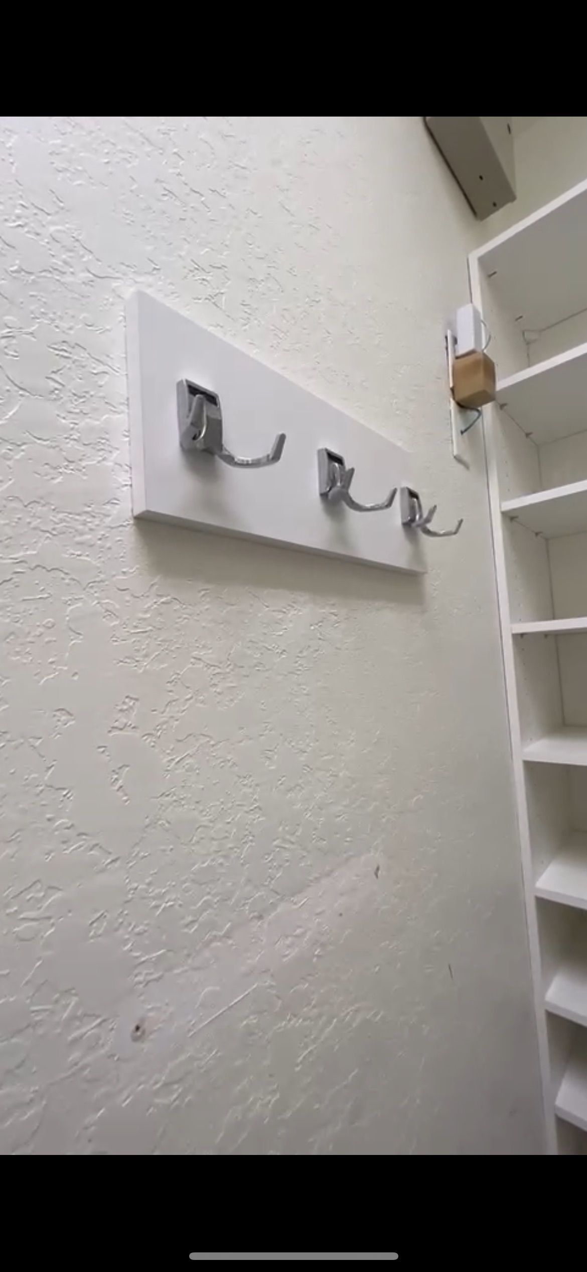 A white coat rack is hanging on a white wall next to a shelf.