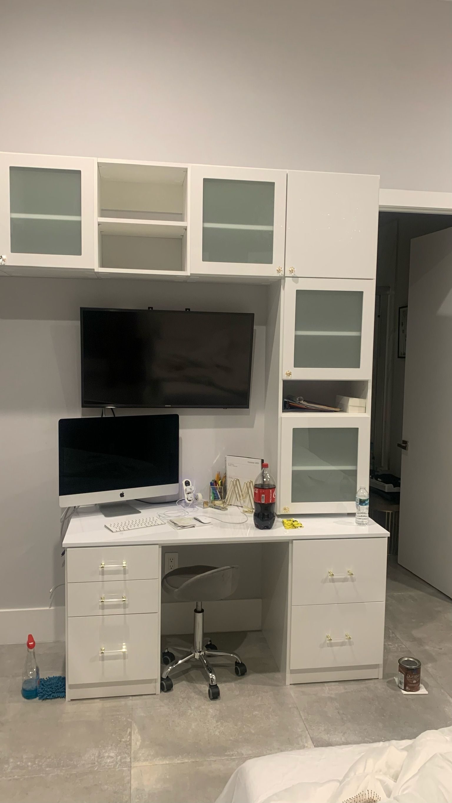 There is a desk with a computer on it and a television on the wall.