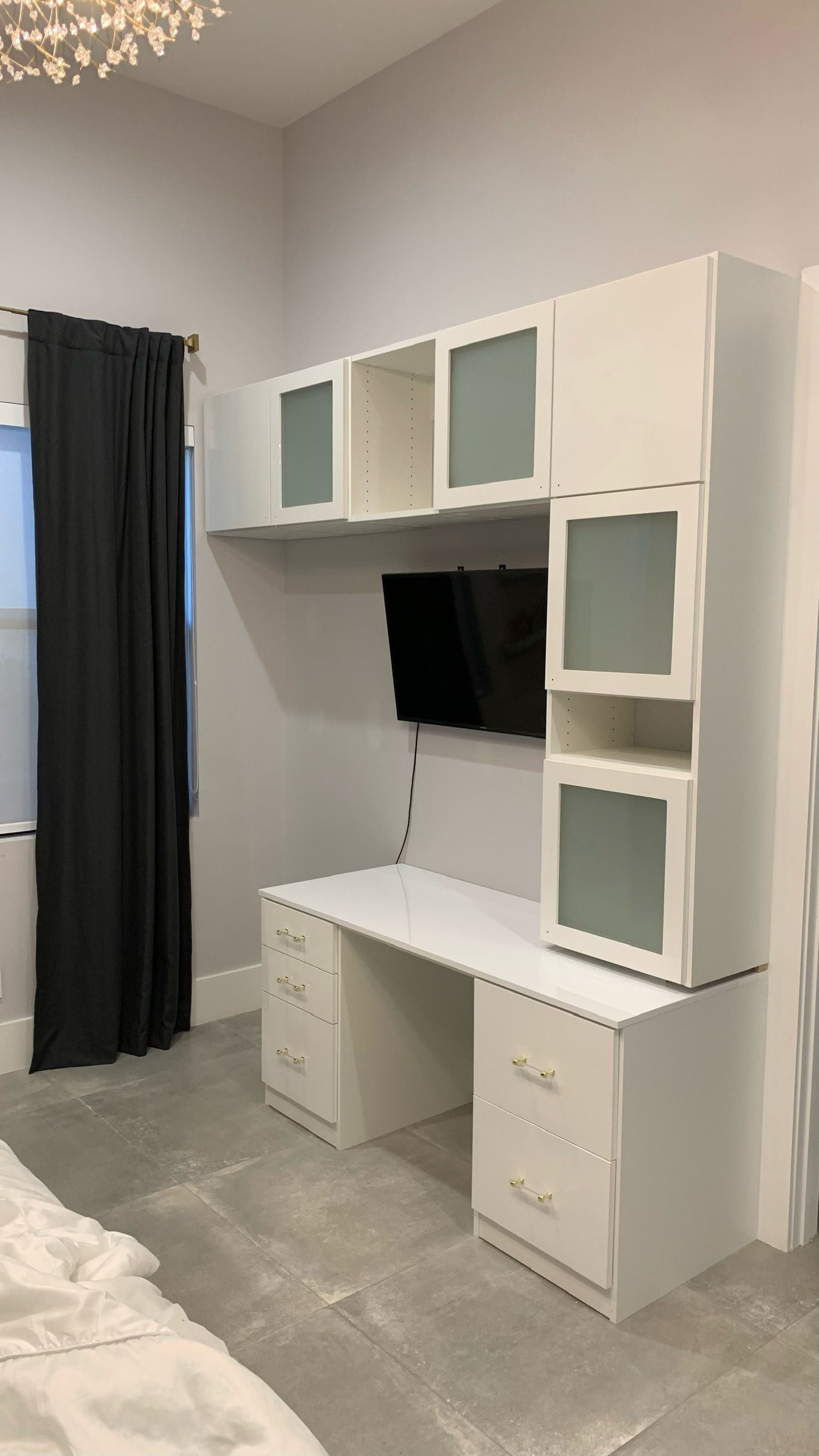 A bedroom with a desk , cabinets , drawers and a television.