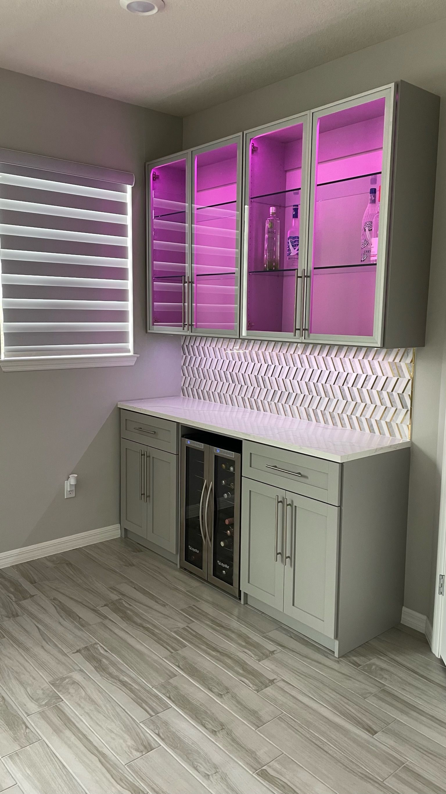 A kitchen with purple lights on the cabinets and a wine cooler.
