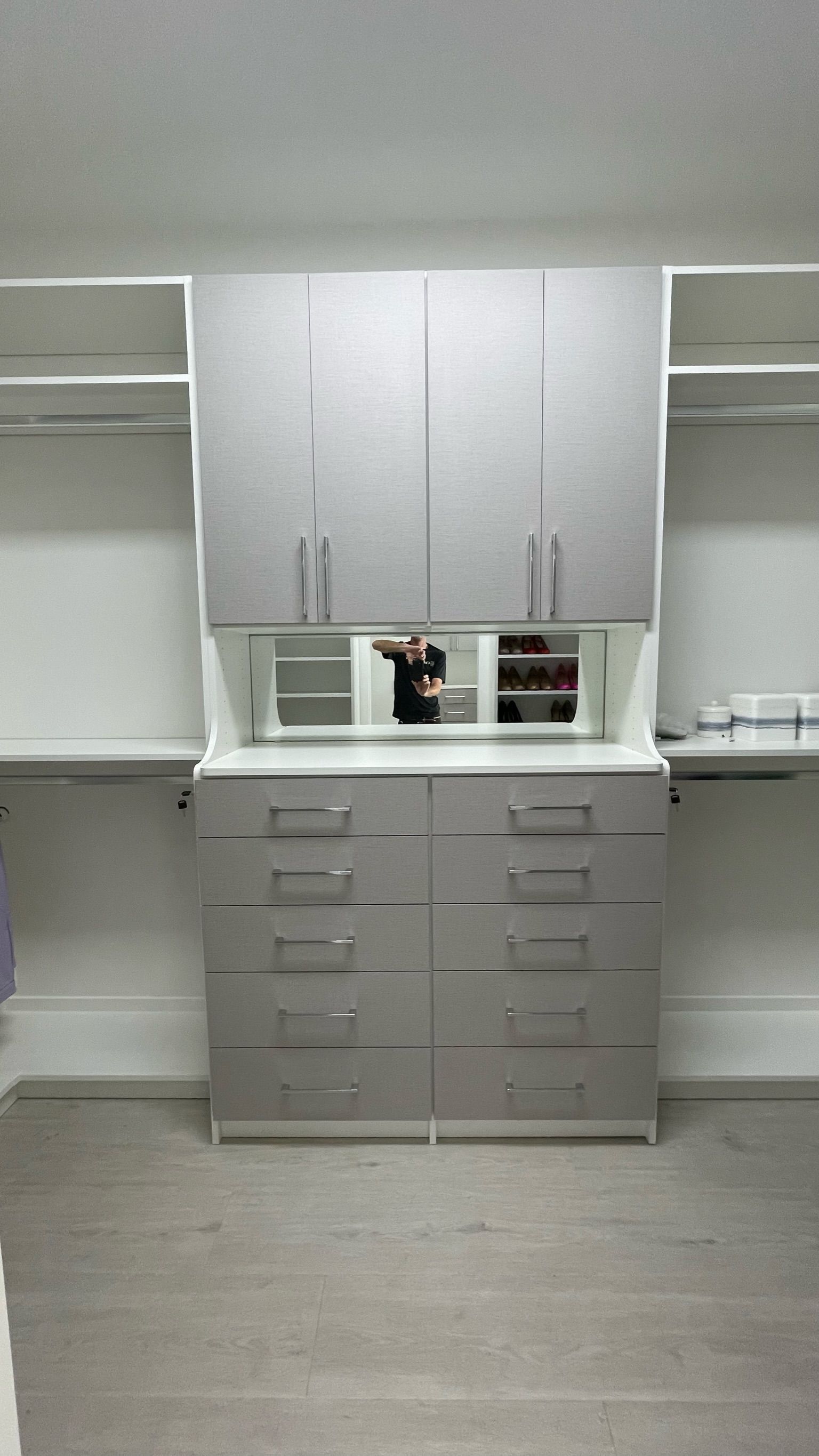 A walk in closet with gray cabinets and drawers and a mirror.