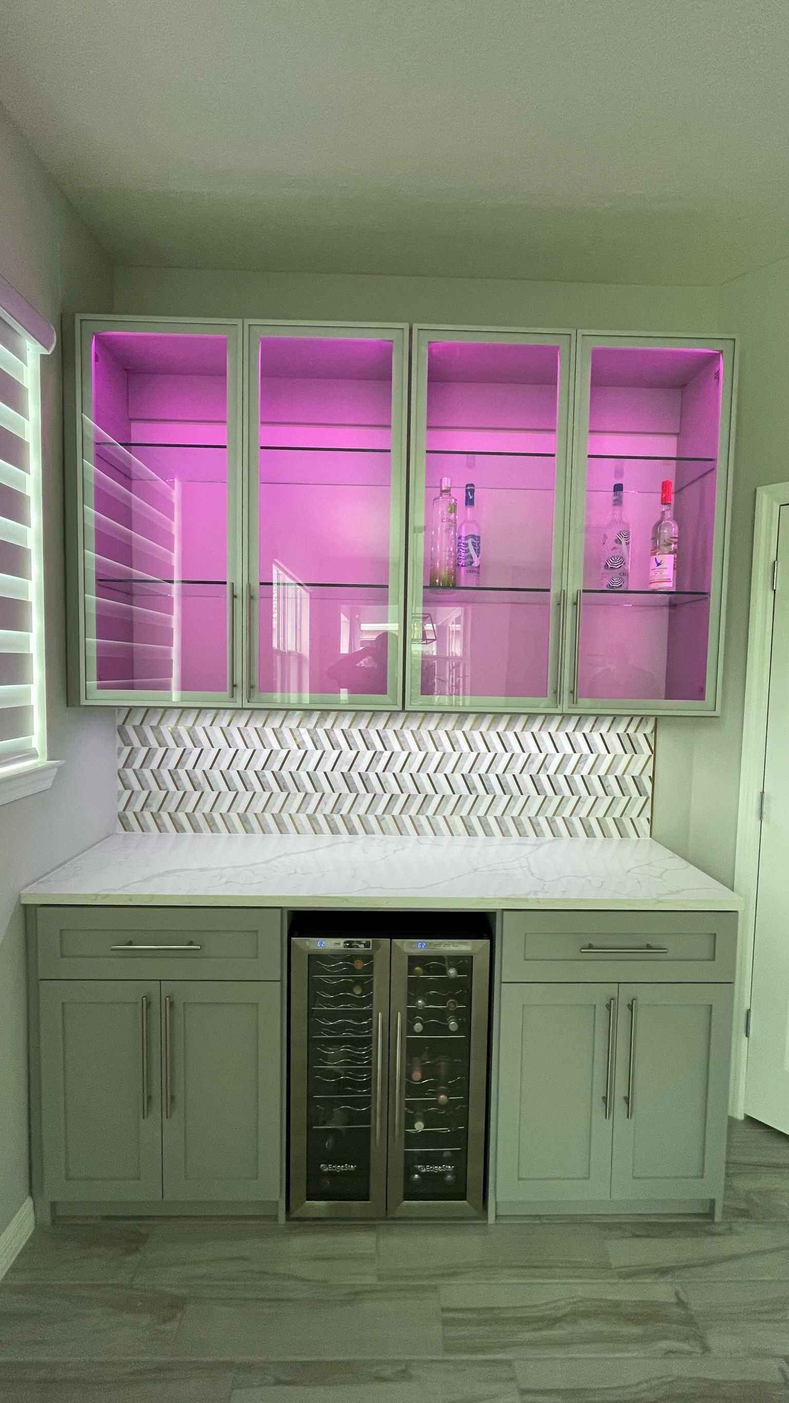 A kitchen with a wine cooler and a bar with purple lights.