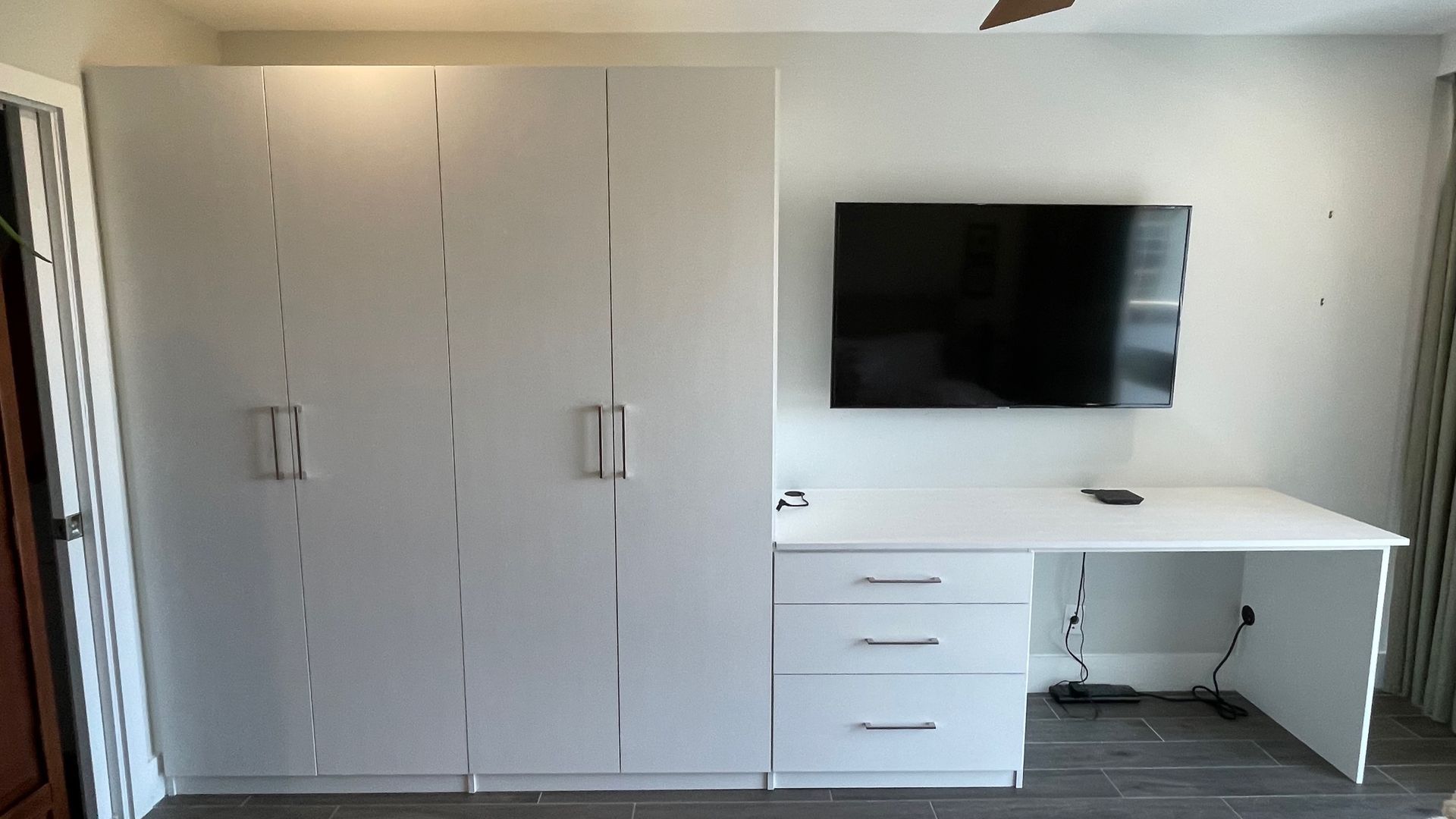 A room with a desk and a flat screen tv on the wall.