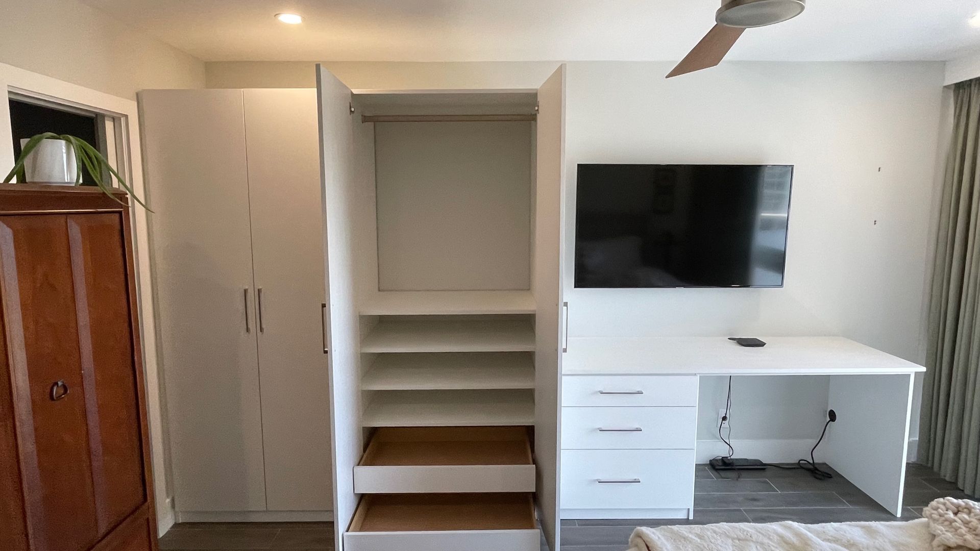 A bedroom with a closet , desk , television and a ceiling fan.