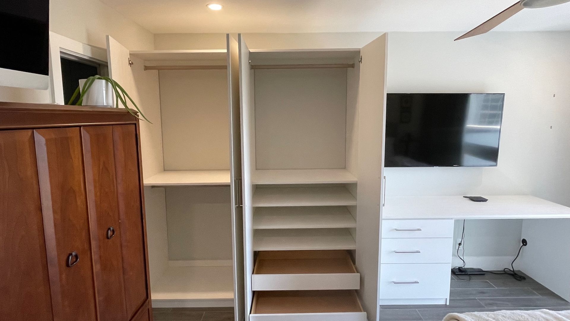 A bedroom with a closet , desk , television and a ceiling fan.