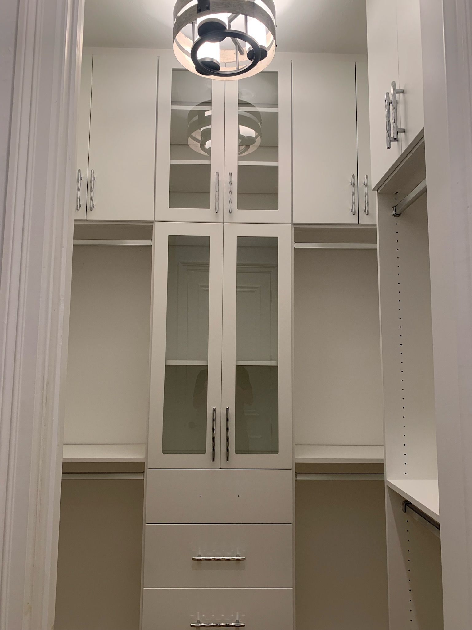 A walk in closet with white cabinets and glass doors.