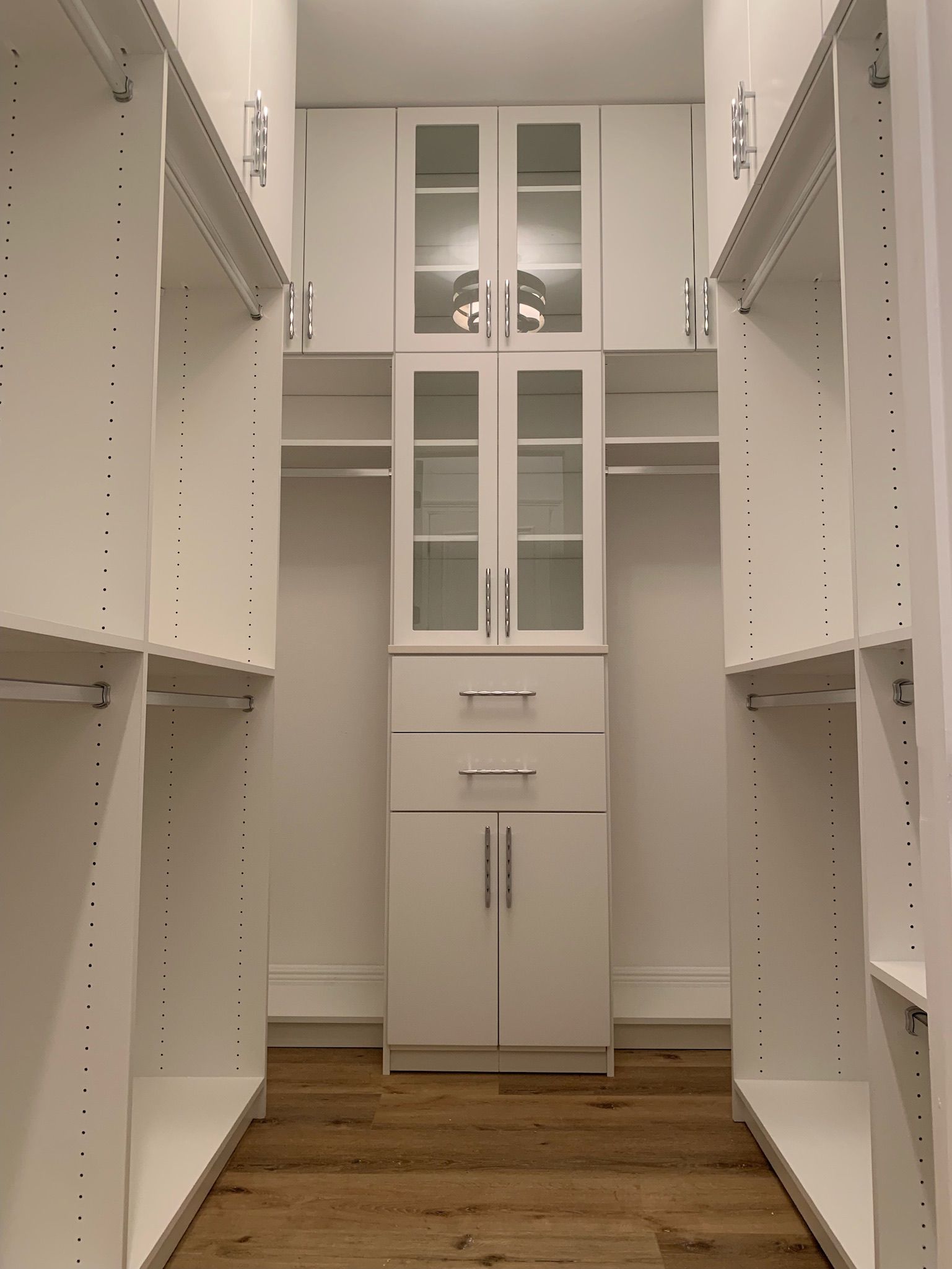 A walk in closet with white cabinets and glass doors