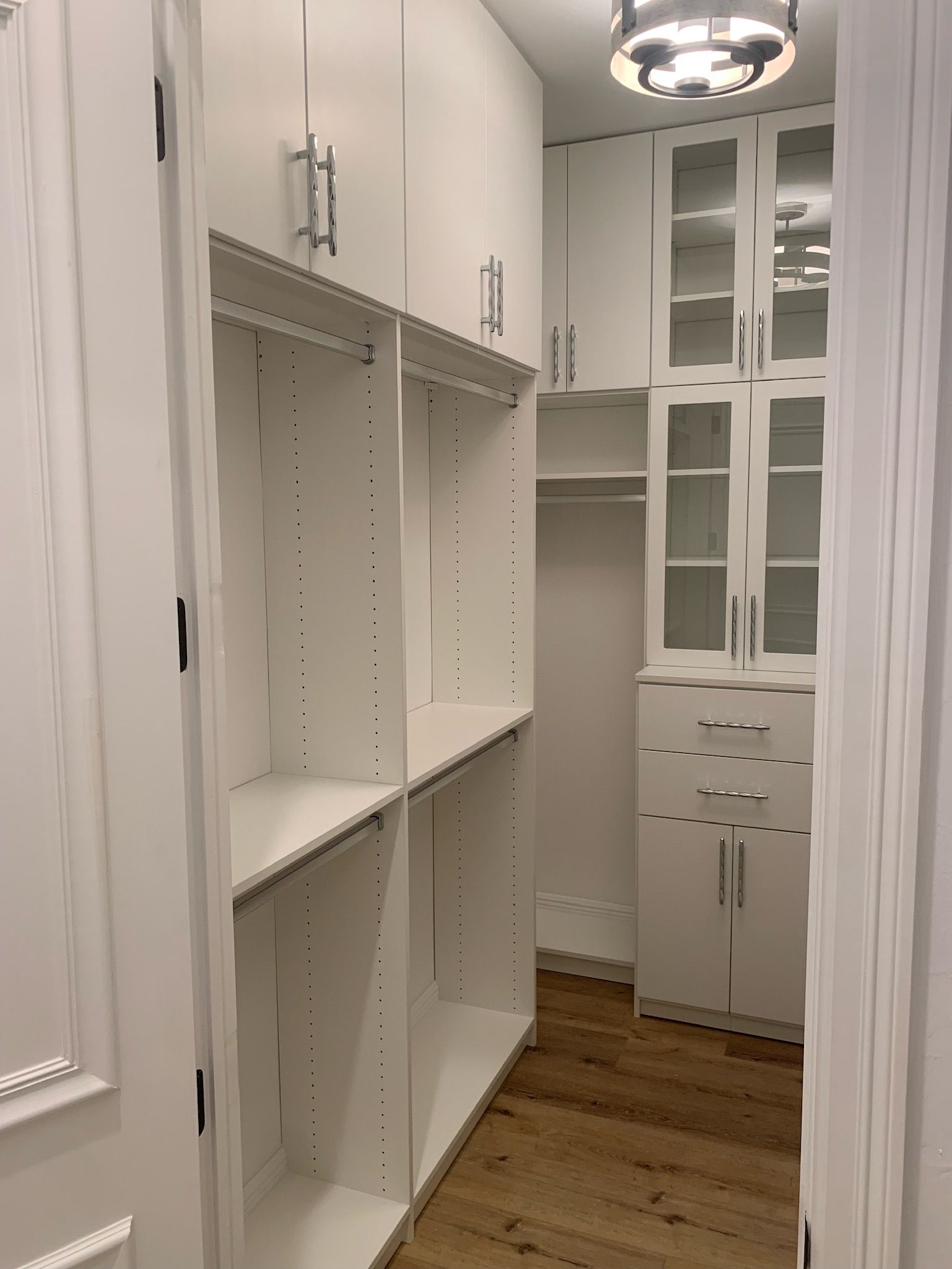 A walk in closet with white cabinets and glass doors.