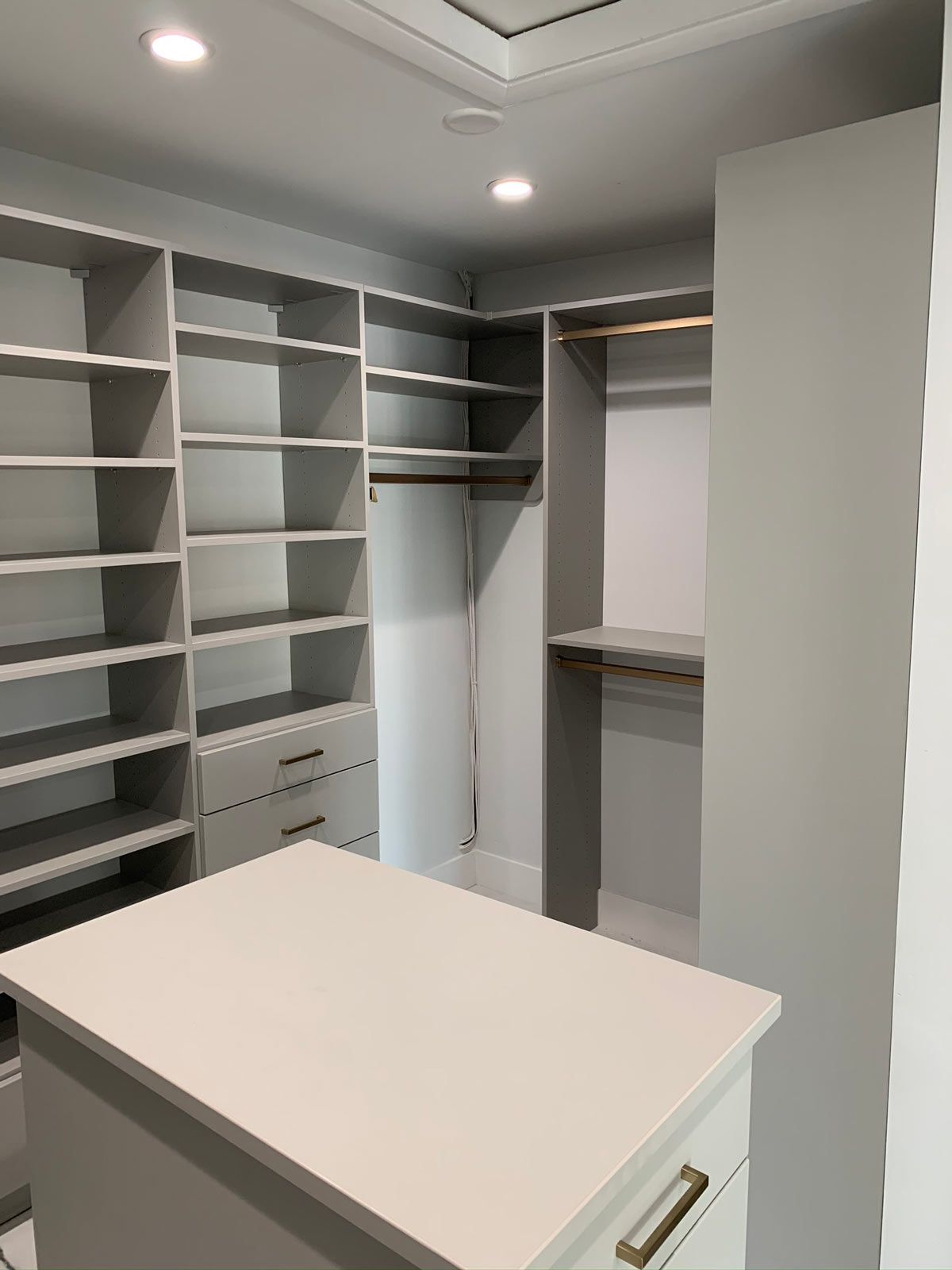 A walk in closet with lots of shelves and drawers and a large island in the middle.