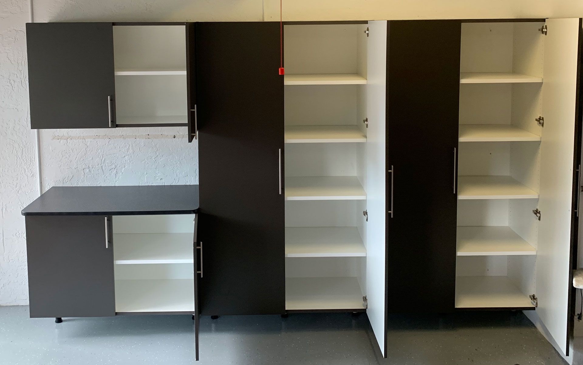 A kitchen with black cabinets and white shelves with the doors open.