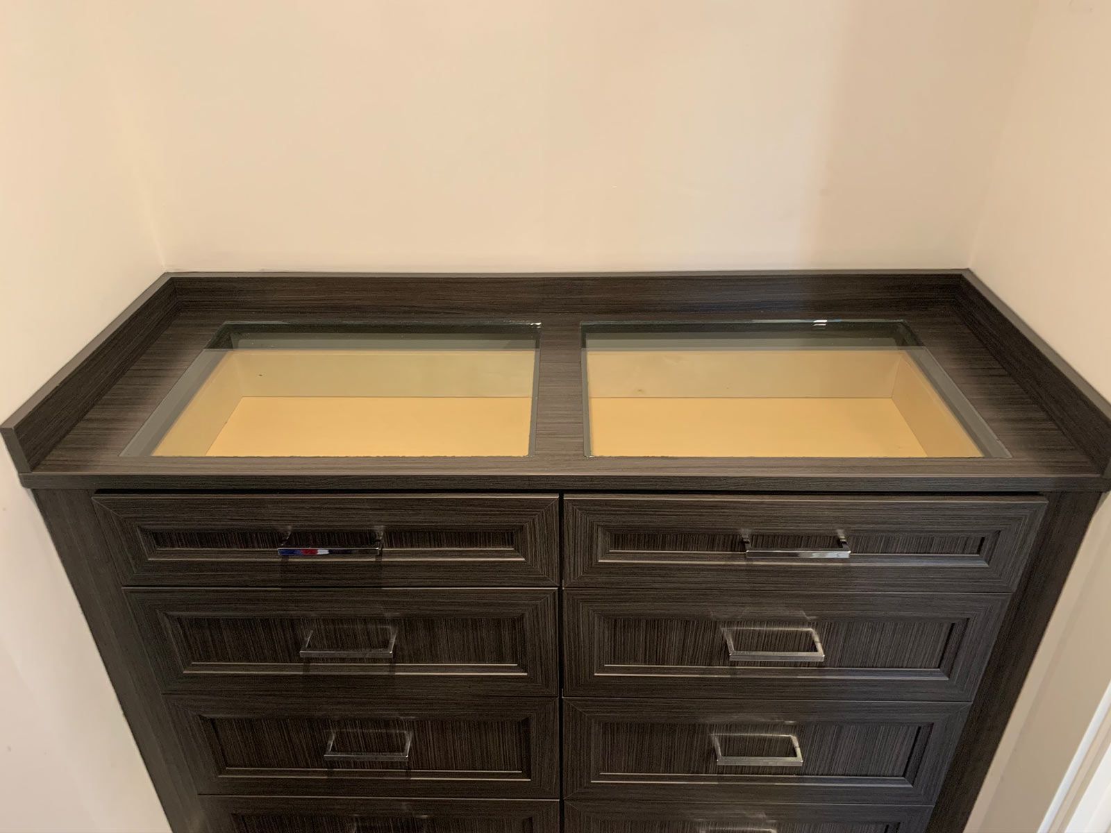 A black dresser with a glass top and drawers in a room.