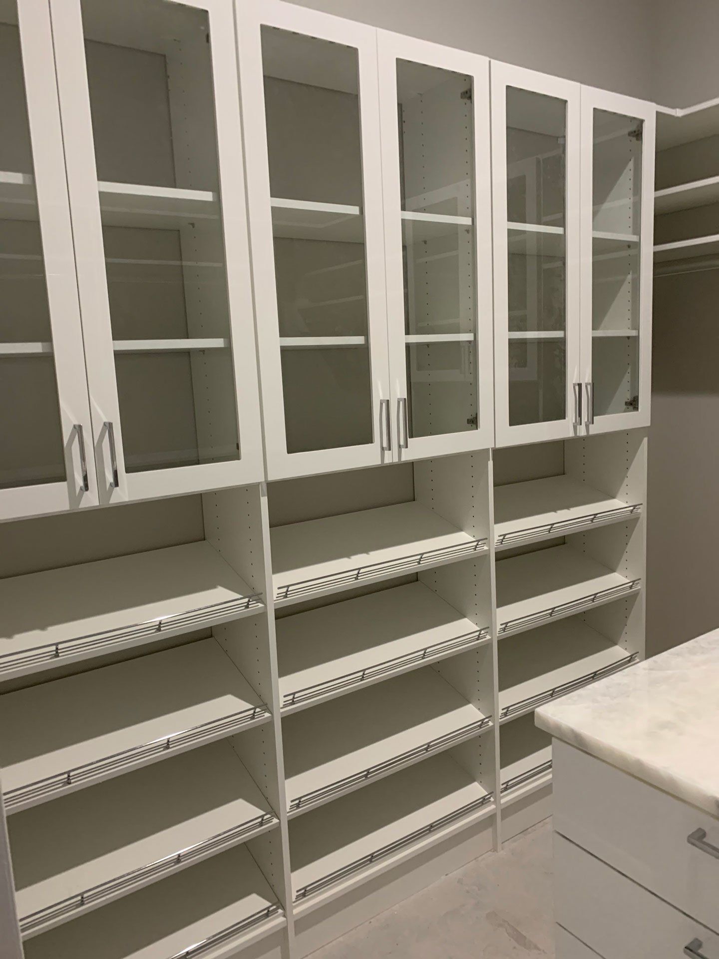A walk in closet with white shelves and glass doors.