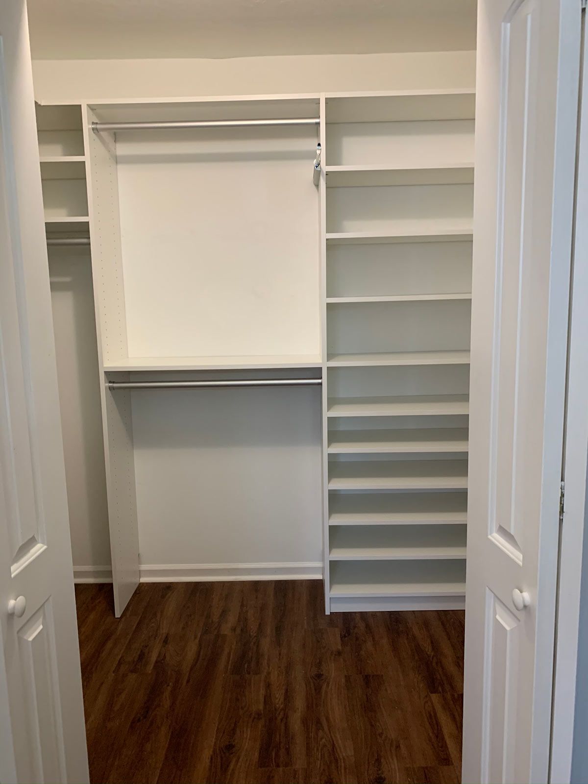 A walk in closet with white shelves and a wooden floor.