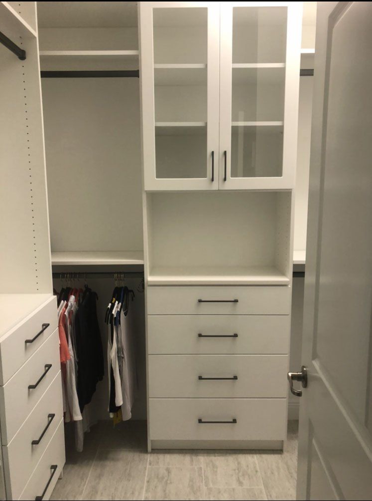 A walk in closet with white cabinets and drawers