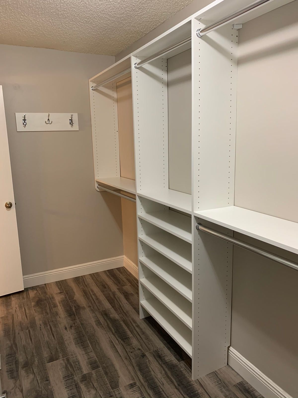 A walk in closet with wooden floors and white shelves.