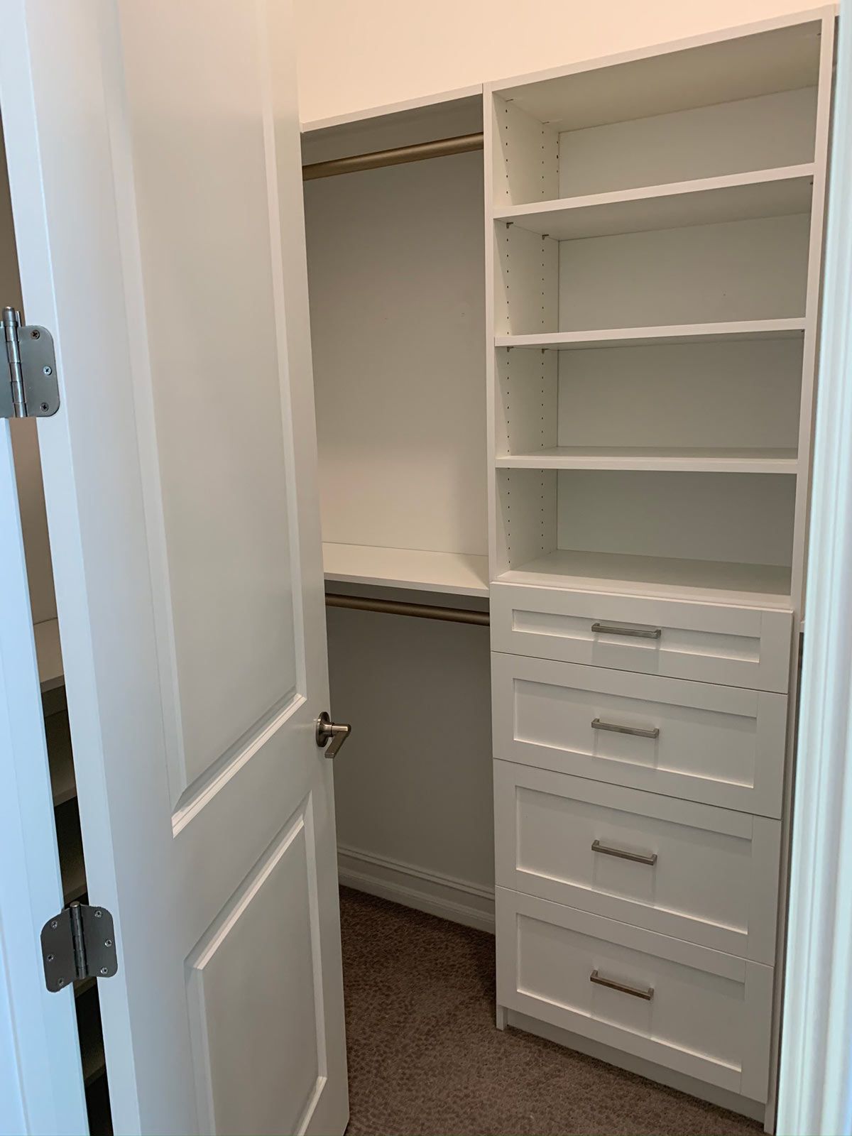 A walk in closet with white shelves and drawers and a door open.