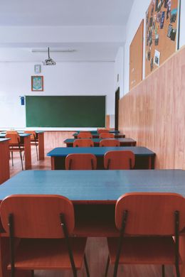 Empty classroom with rows of desks and chairs, a chalkboard, and corkboard on the wall.