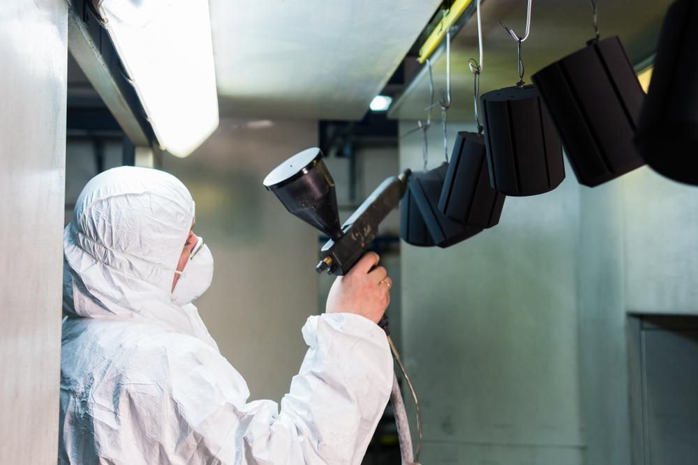 A Man in a White Suit and Mask is Spraying Powder Paint on a Black Object — Alamo Powder Coaters in Moss Vale, NSW