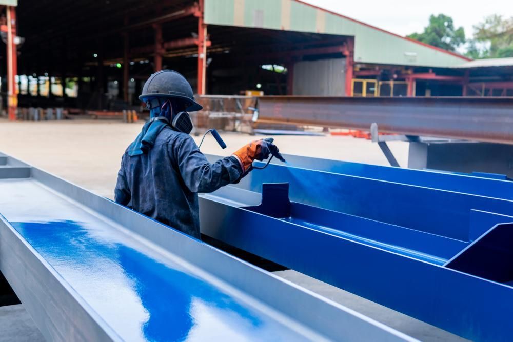A Man is Spray Painting a Blue Metal Structure in a Factory — Alamo Powder Coaters in Moss Vale, NSW