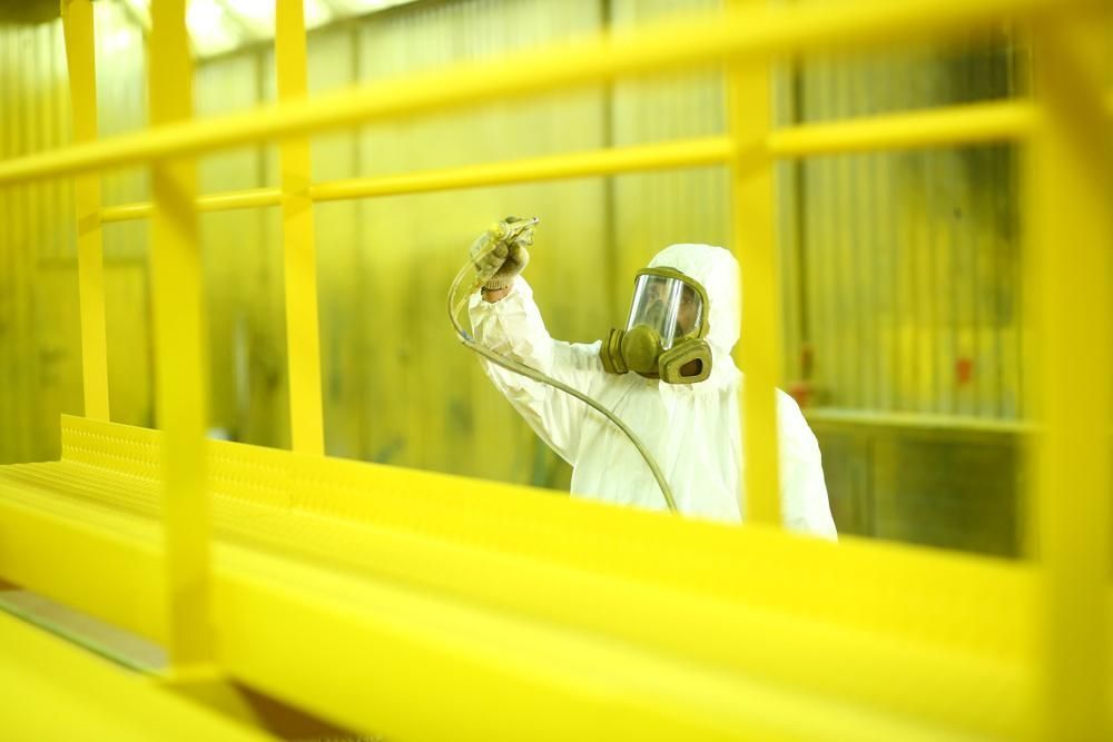 A Man Wearing a Gas Mask is Spraying Yellow Paint on a Yellow Railing — Alamo Powder Coaters in Moss Vale, NSW