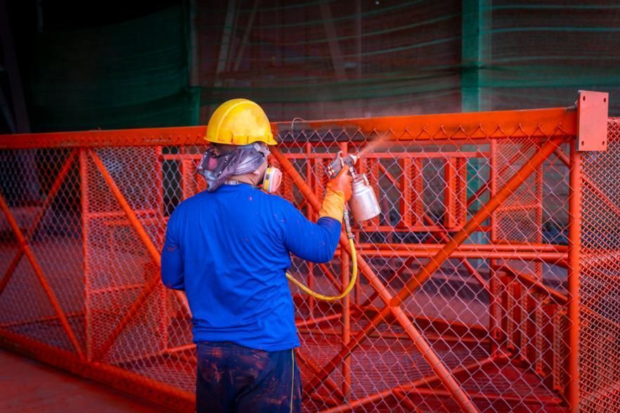 A Man is Spraying Orange Paint on a Metal Structure — Alamo Powder Coaters in Mittagong, NSW
