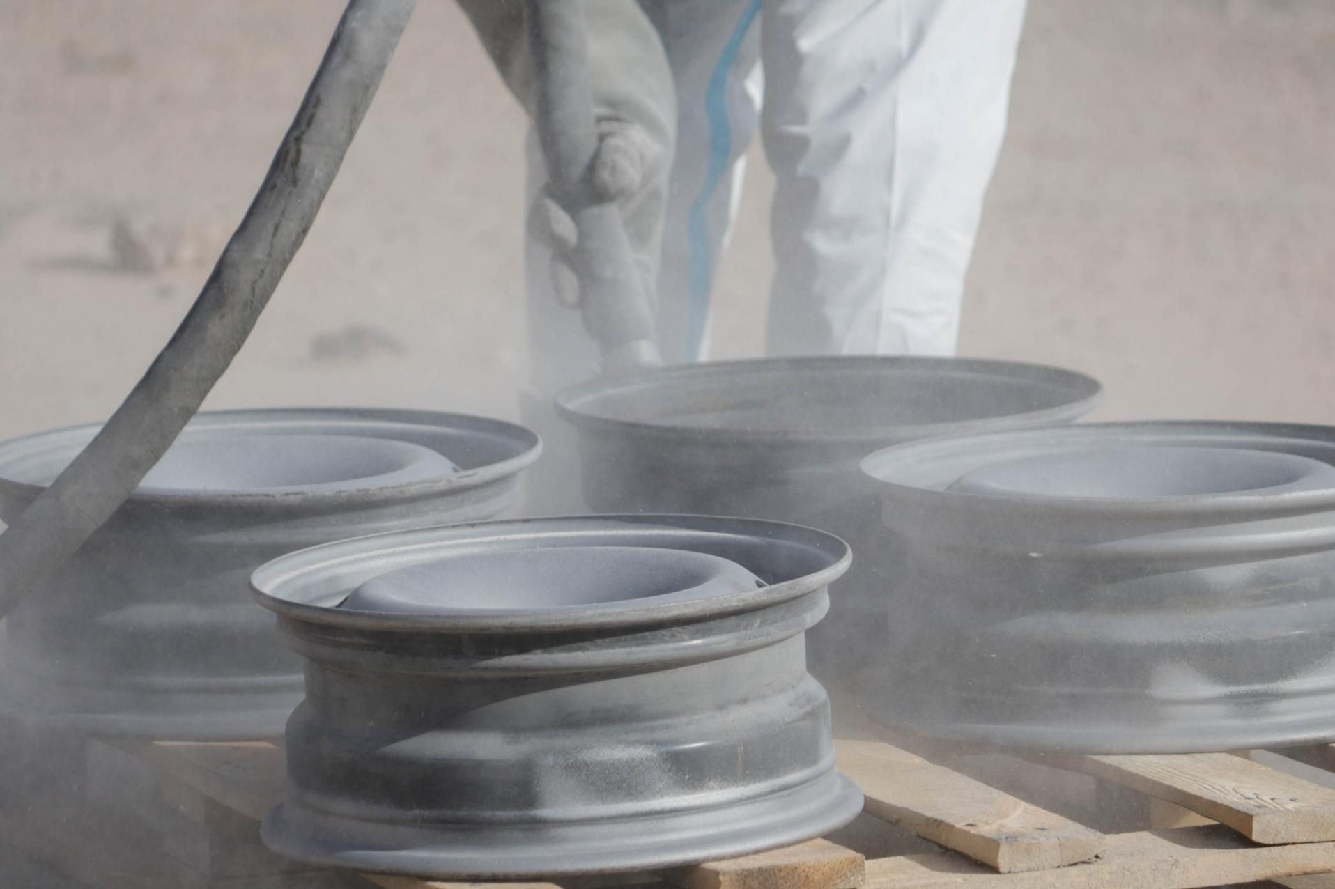 A Person is Sandblasting a Bunch of Wheels on a Wooden Pallet — Alamo Powder Coaters in Bowral, NSW