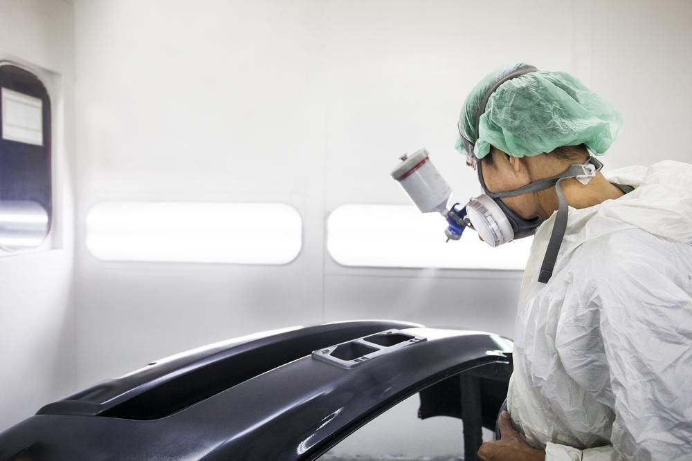 A Man Wearing a Mask is Spray Painting a Car Bumper — Alamo Powder Coaters in Bowral, NSW