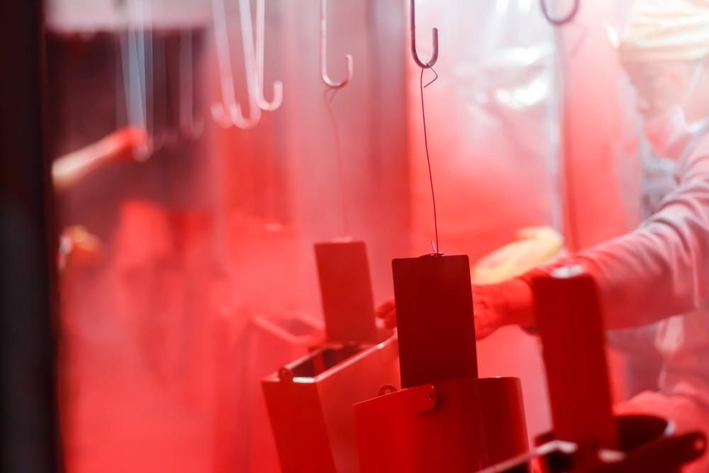 A Person is Painting a Piece of Metal With Red Paint — Alamo Powder Coaters in Mittagong, NSW