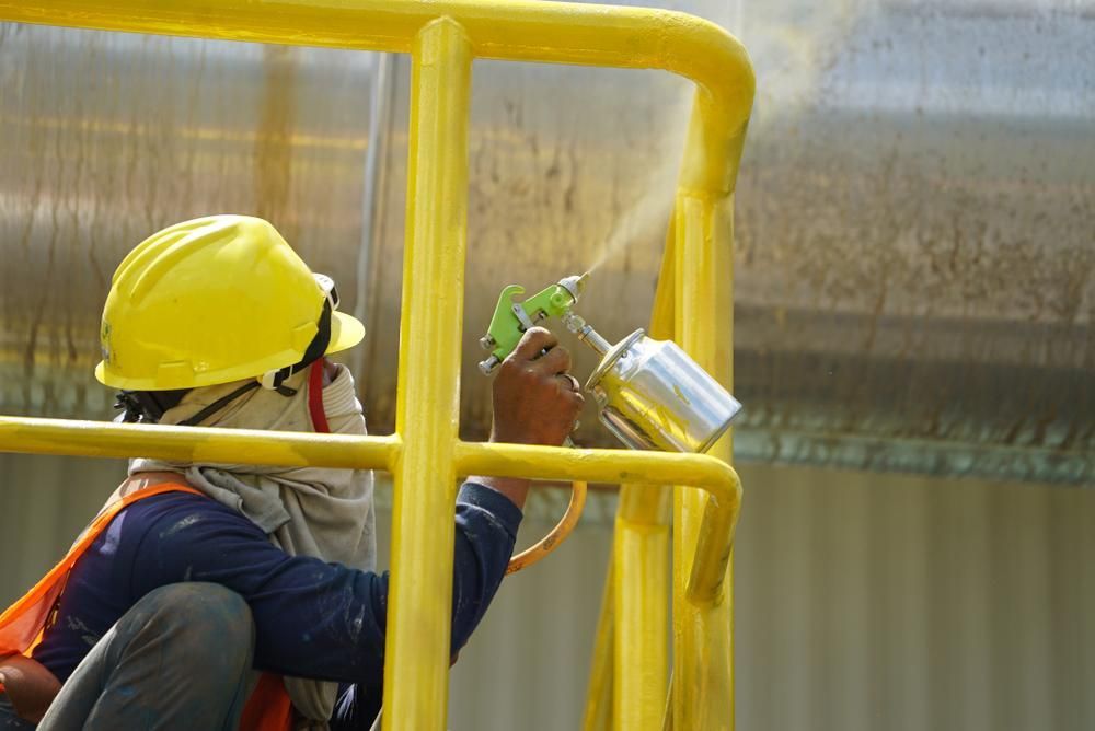 A Man is Sitting on a Ladder Spraying Paint on a Wall — Alamo Powder Coaters in Bowral, NSW