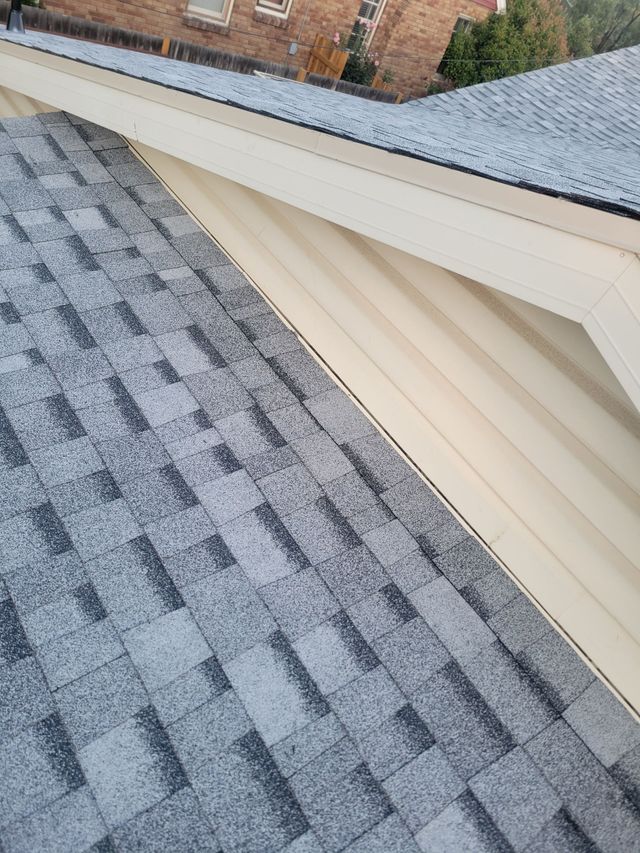 Snow-dusted gray shingle roof beside cream siding and a brick house wall