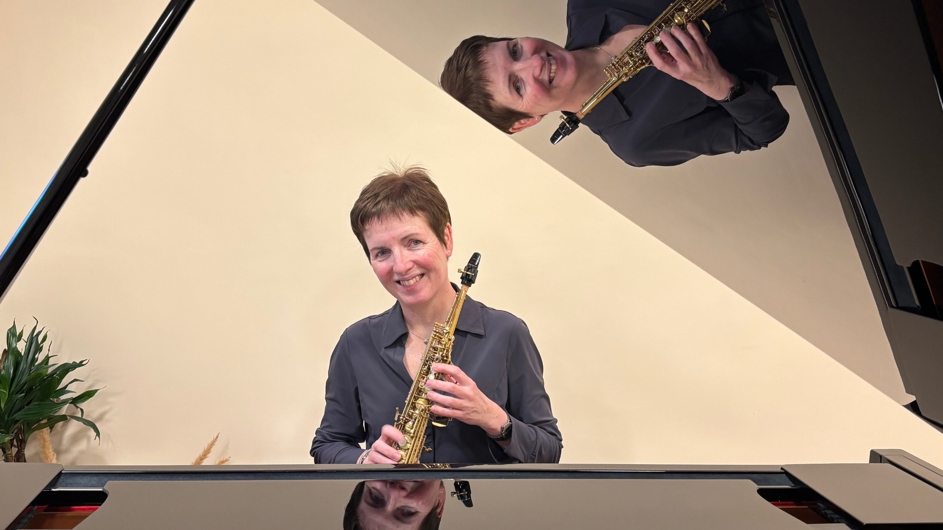 Vrouw met een saxofoon in haar handen, lachend, met haar spiegelbeeld erboven; vlakbij een piano.