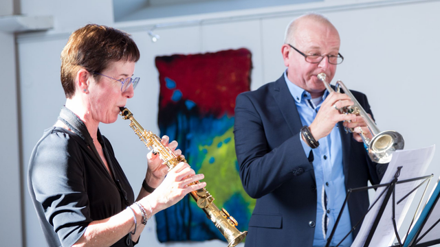 Vrouw speelt saxofoon, man speelt trompet, noten lezen.