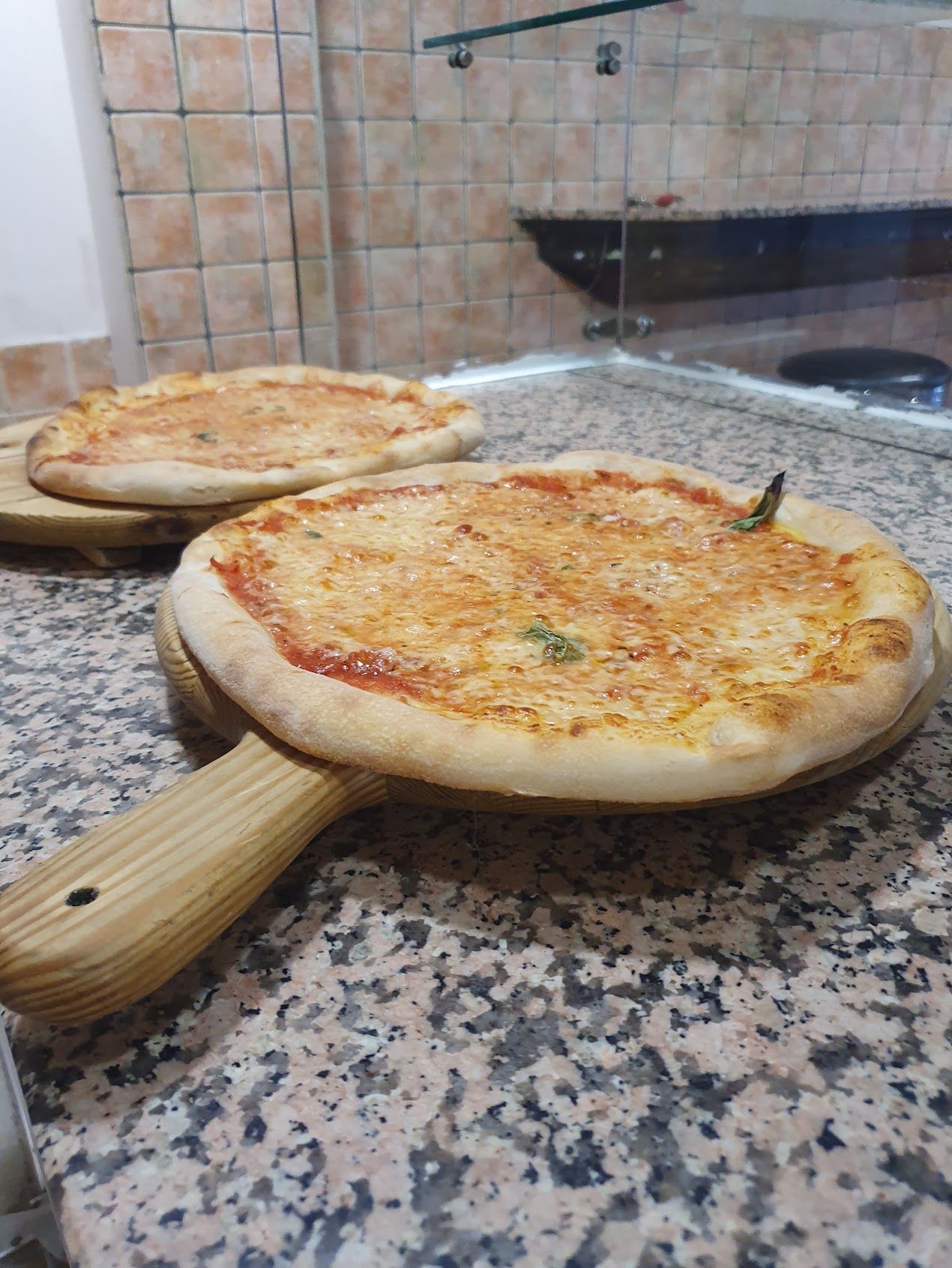Due pizze sono sedute su un tagliere di legno su un bancone.