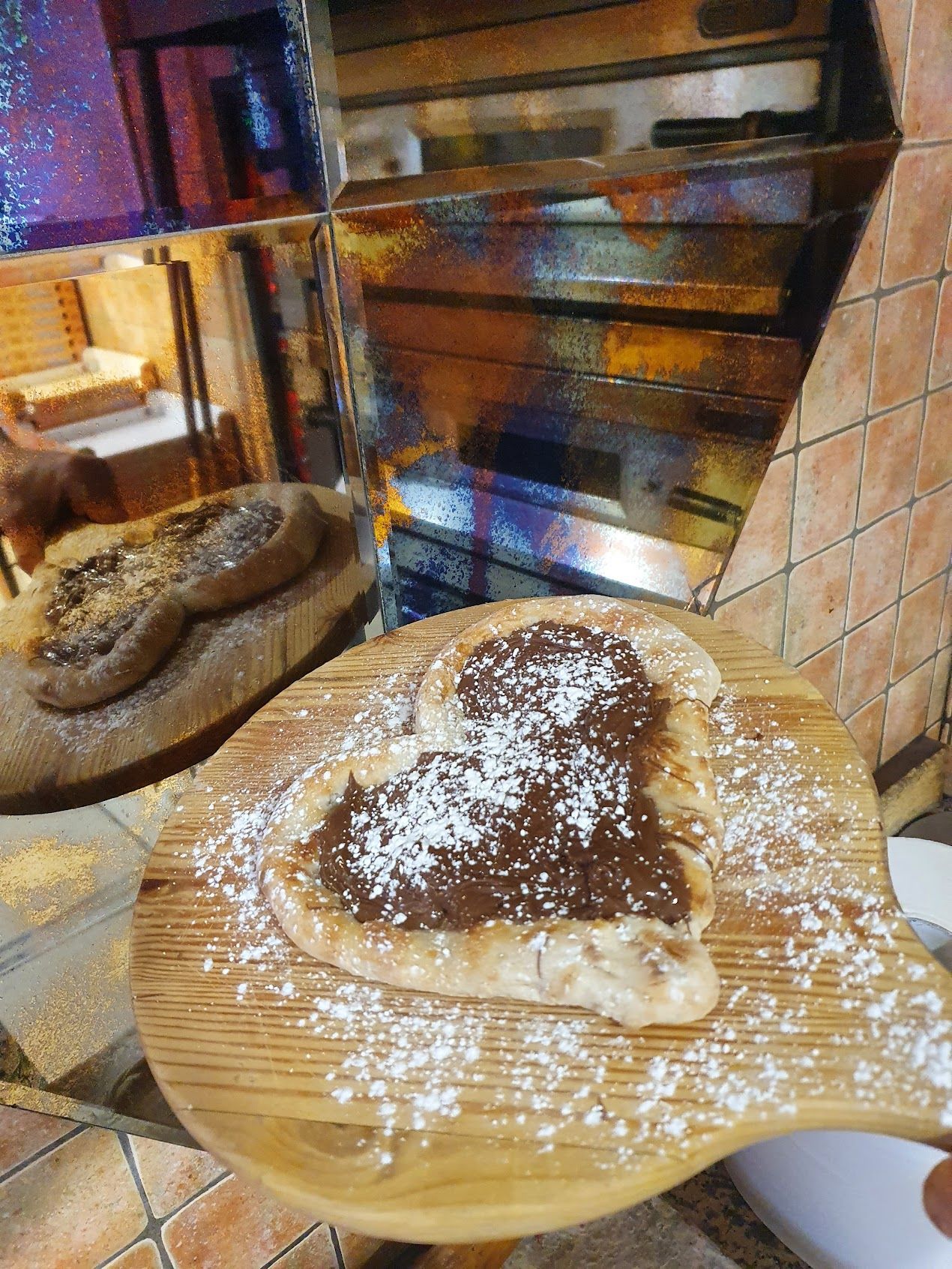 Una pizza a forma di cuore con nutella e zucchero a velo su un tagliere di legno.