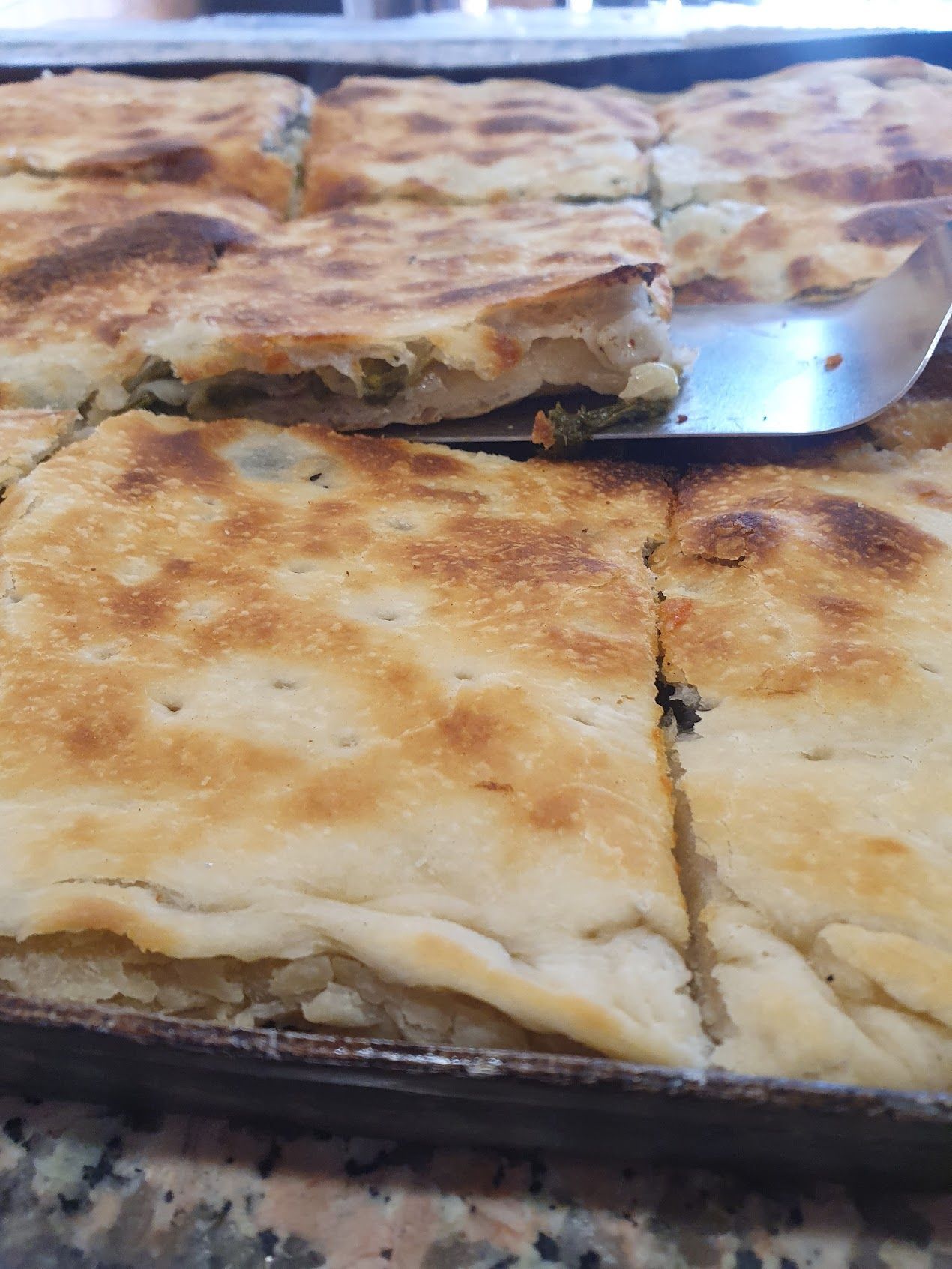 Una pizza viene affettata su una teglia con una spatola.