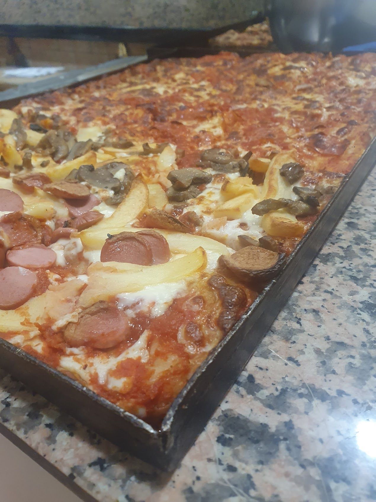 Su un vassoio sul bancone c'è una pizza con patatine fritte, salsiccia, funghi e formaggio.