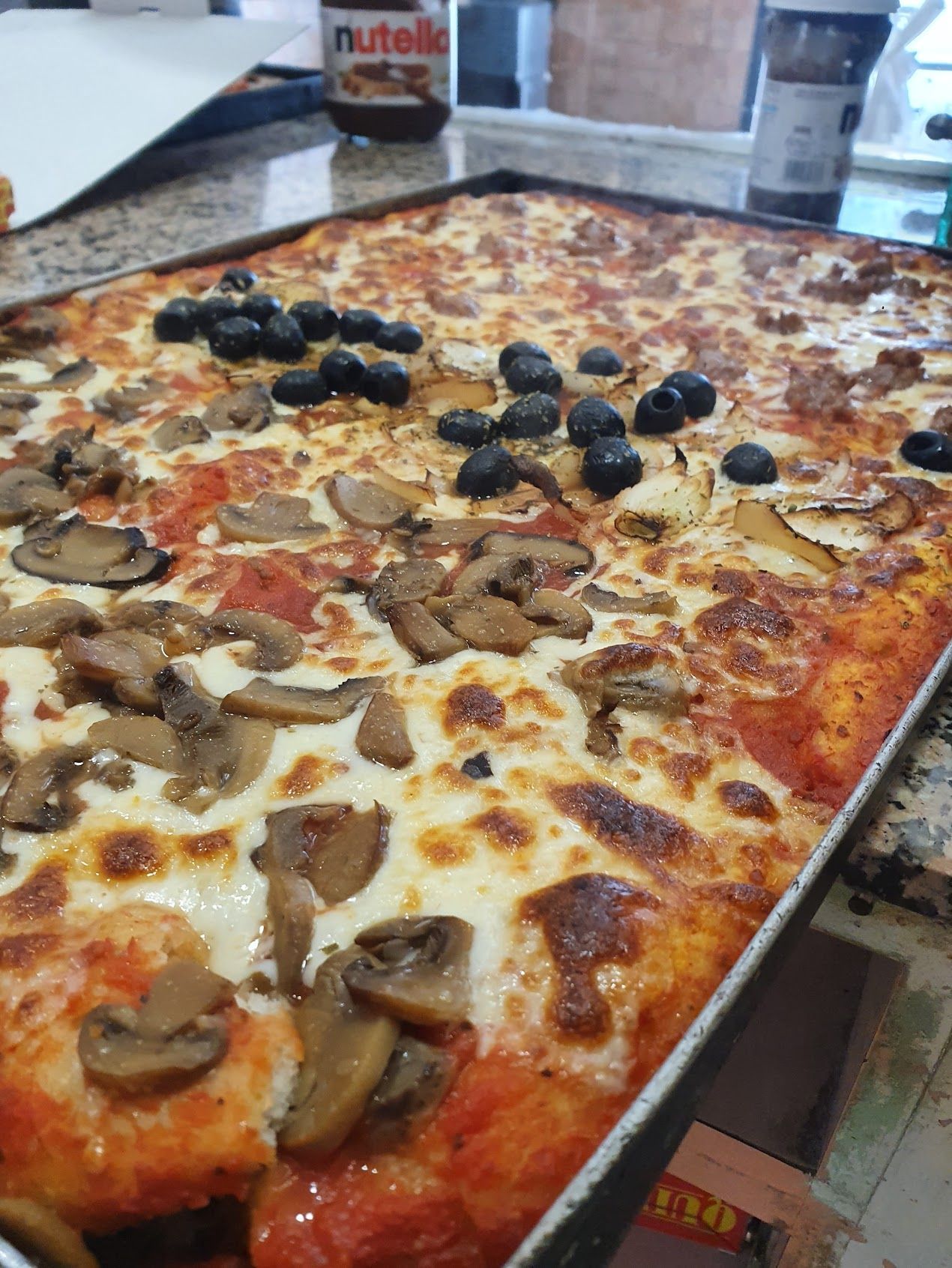 Su un tavolo è seduta una pizza con funghi, olive e formaggio.