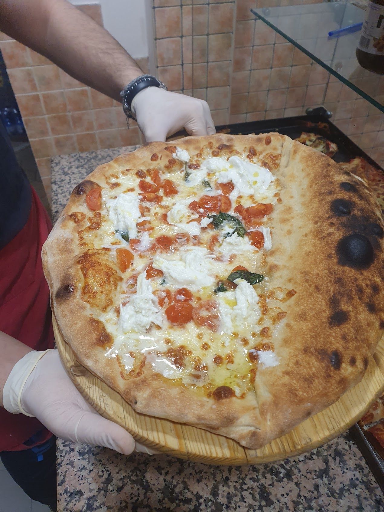 Una persona tiene in mano una pizza su un vassoio di legno.