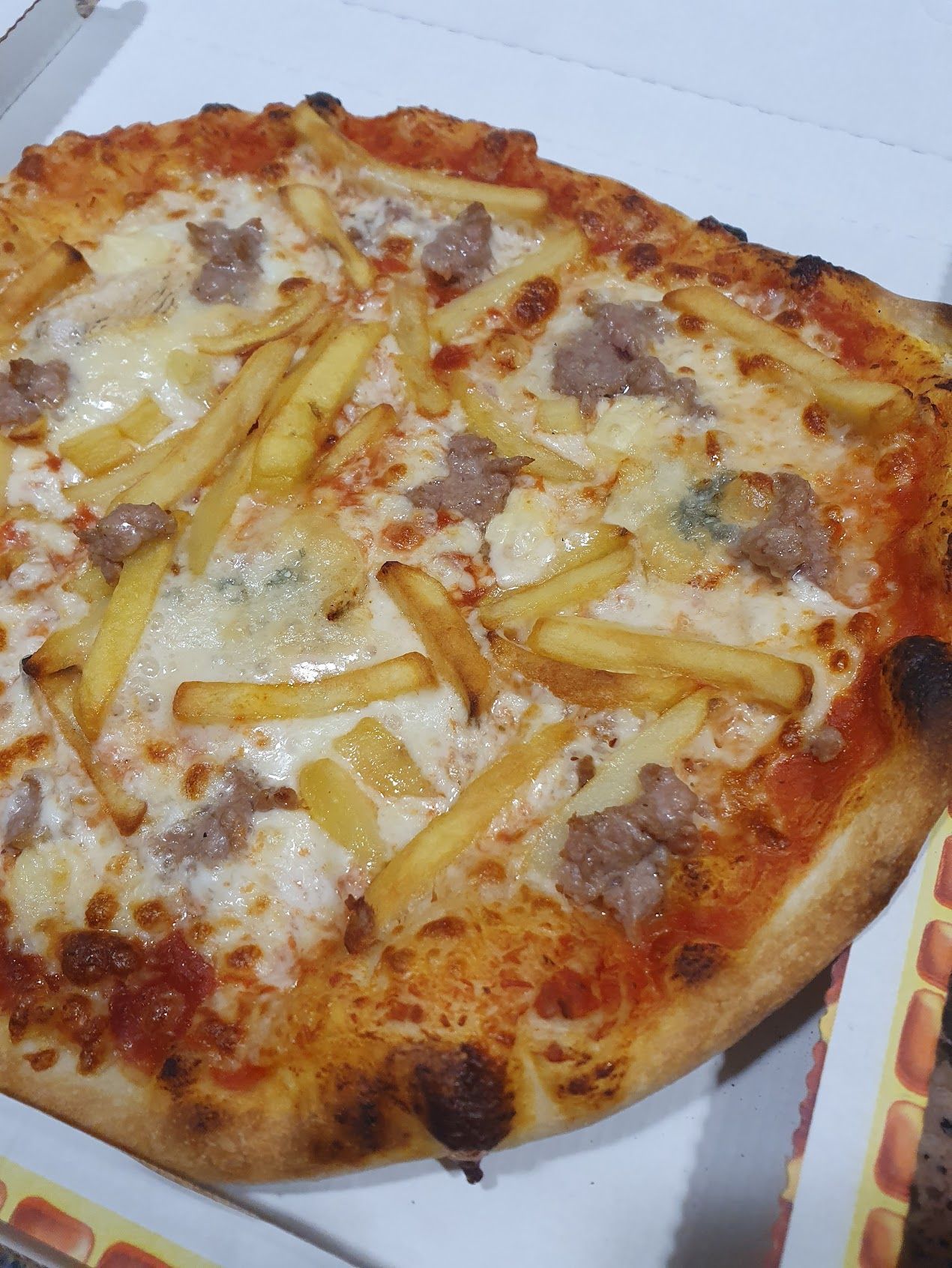 In una scatola c'è una pizza con patatine fritte e salsiccia.