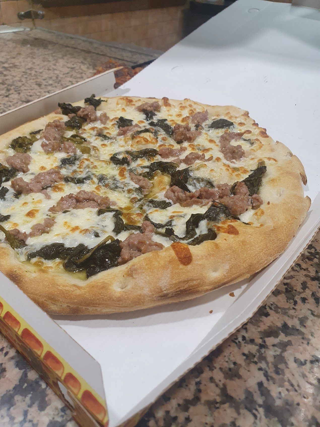In una scatola c'è una pizza con spinaci e salsiccia
