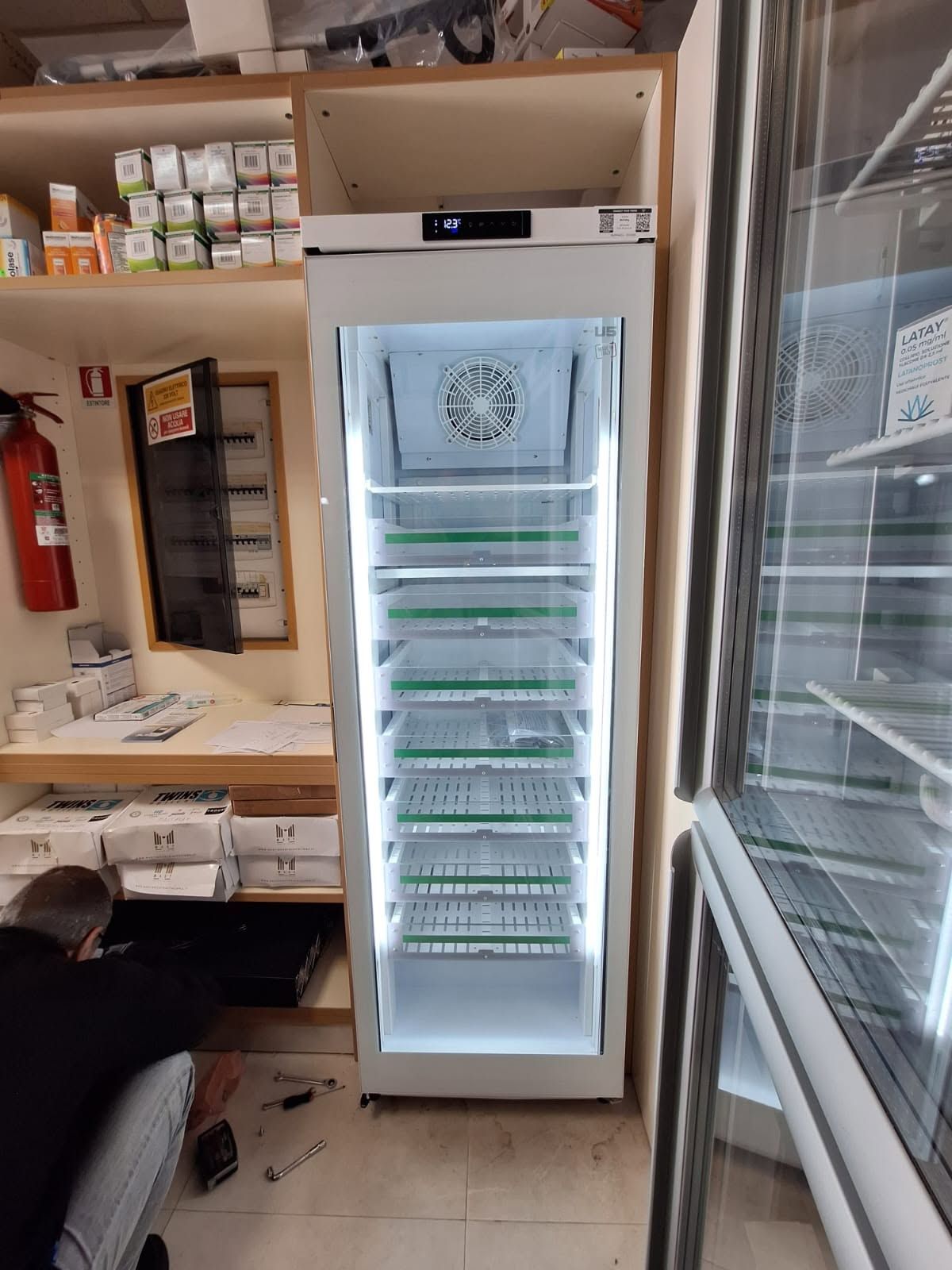 In un'officina, un frigorifero per bevande aperto e acceso, con una persona accovacciata accanto.