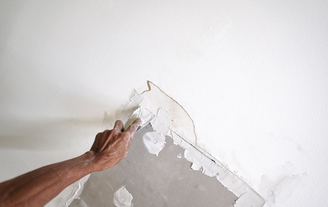 A person is plastering a wall with a trowel.
