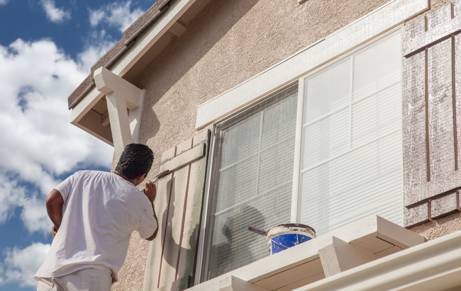 A man is painting a window on the side of a house.