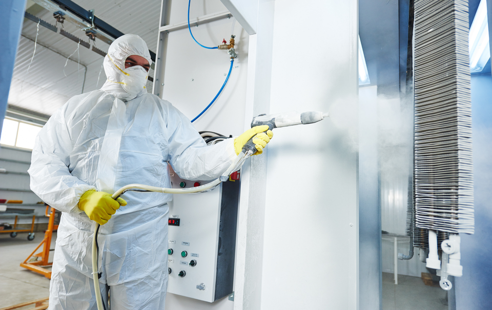 A man in a protective suit is spraying paint on a wall.