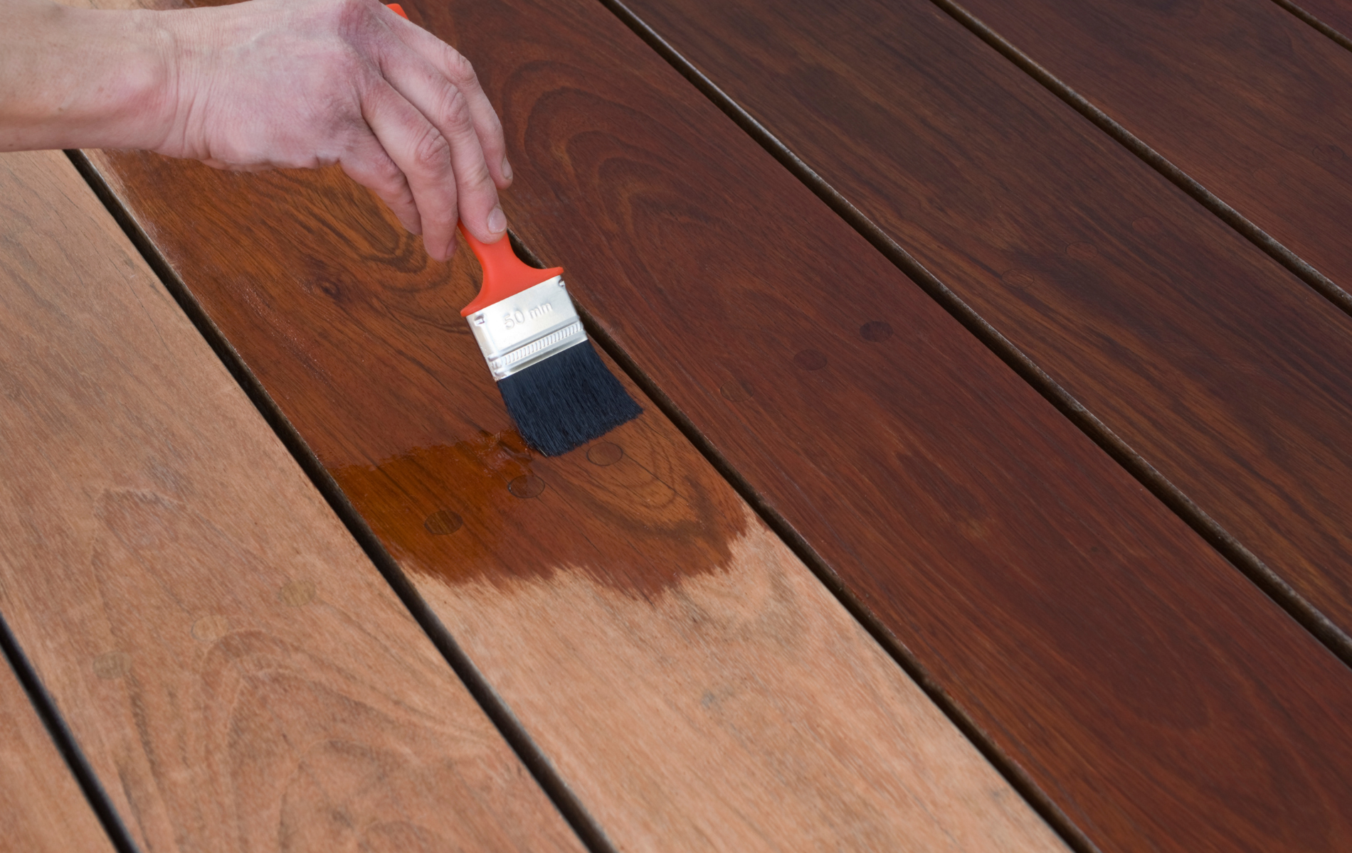 A person is painting a wooden deck with a brush.