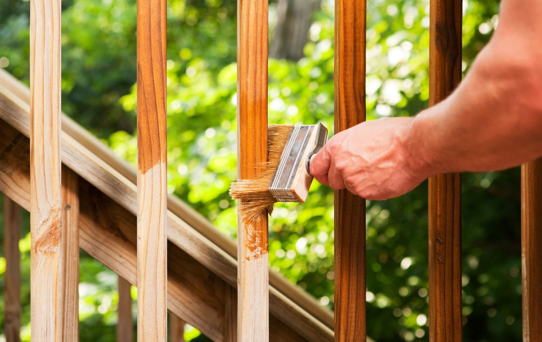A person is painting a wooden railing with a brush.