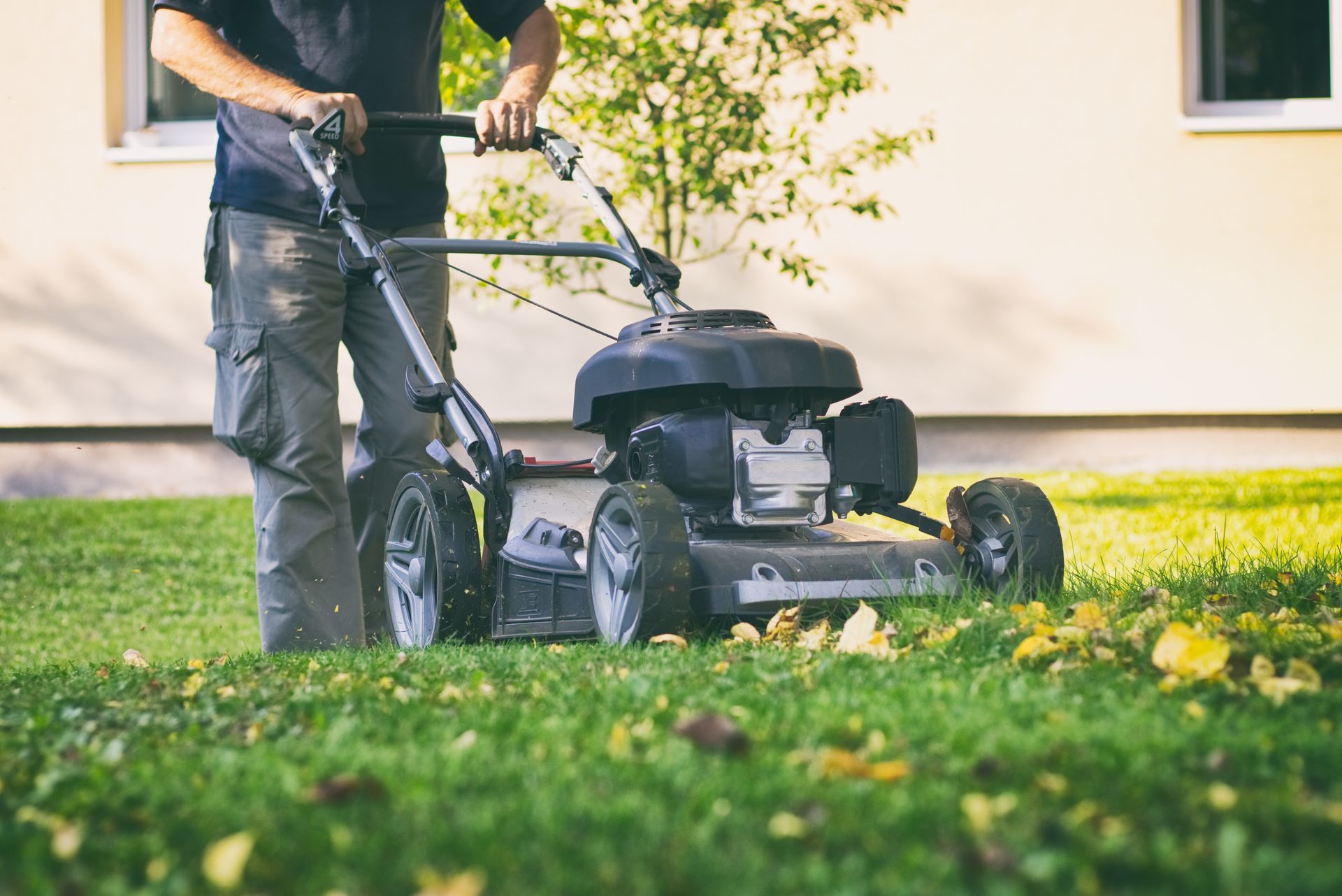 Person mowing a green lawn with a push mower beside a house
