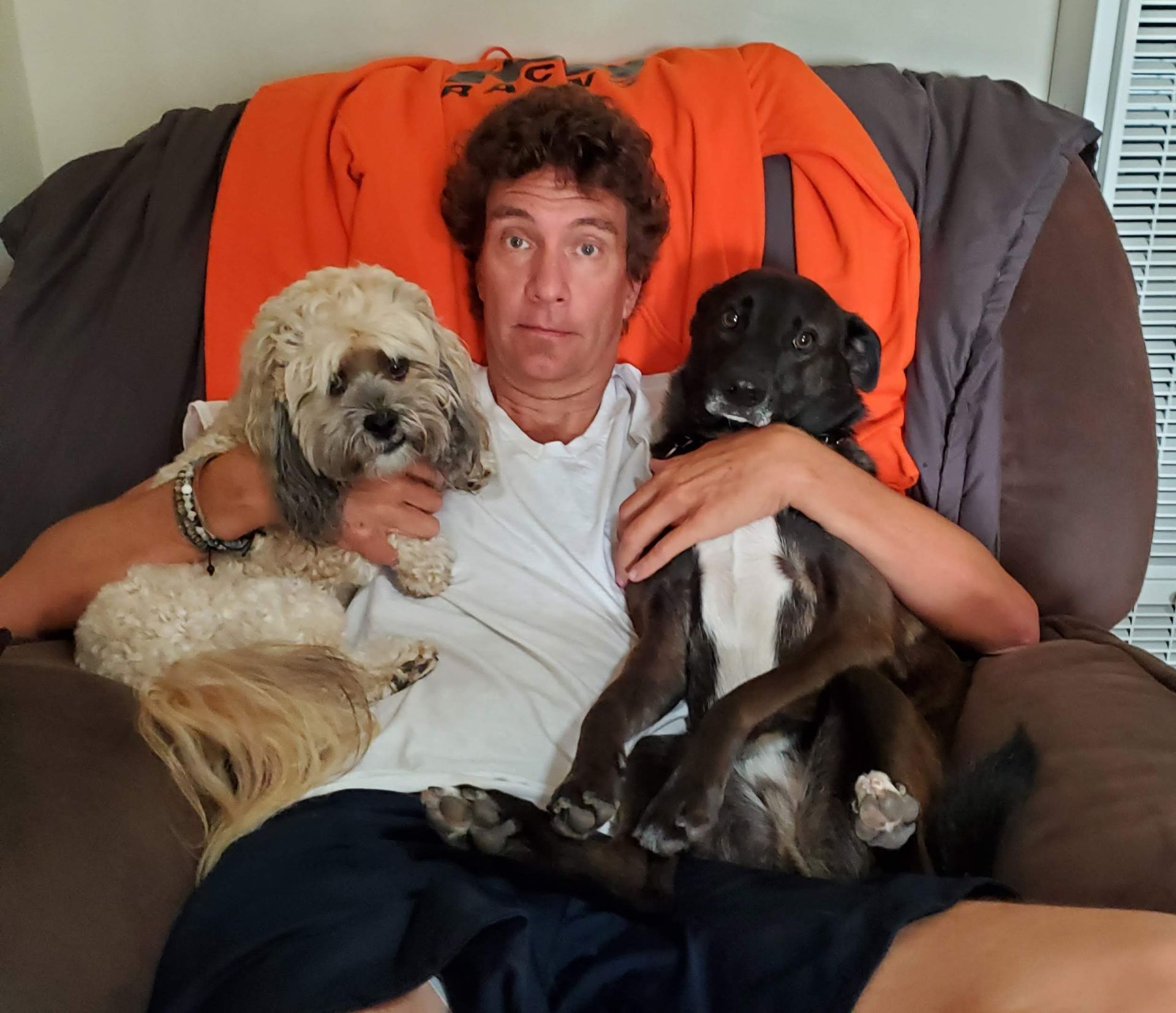 A man is sitting on a couch with two dogs