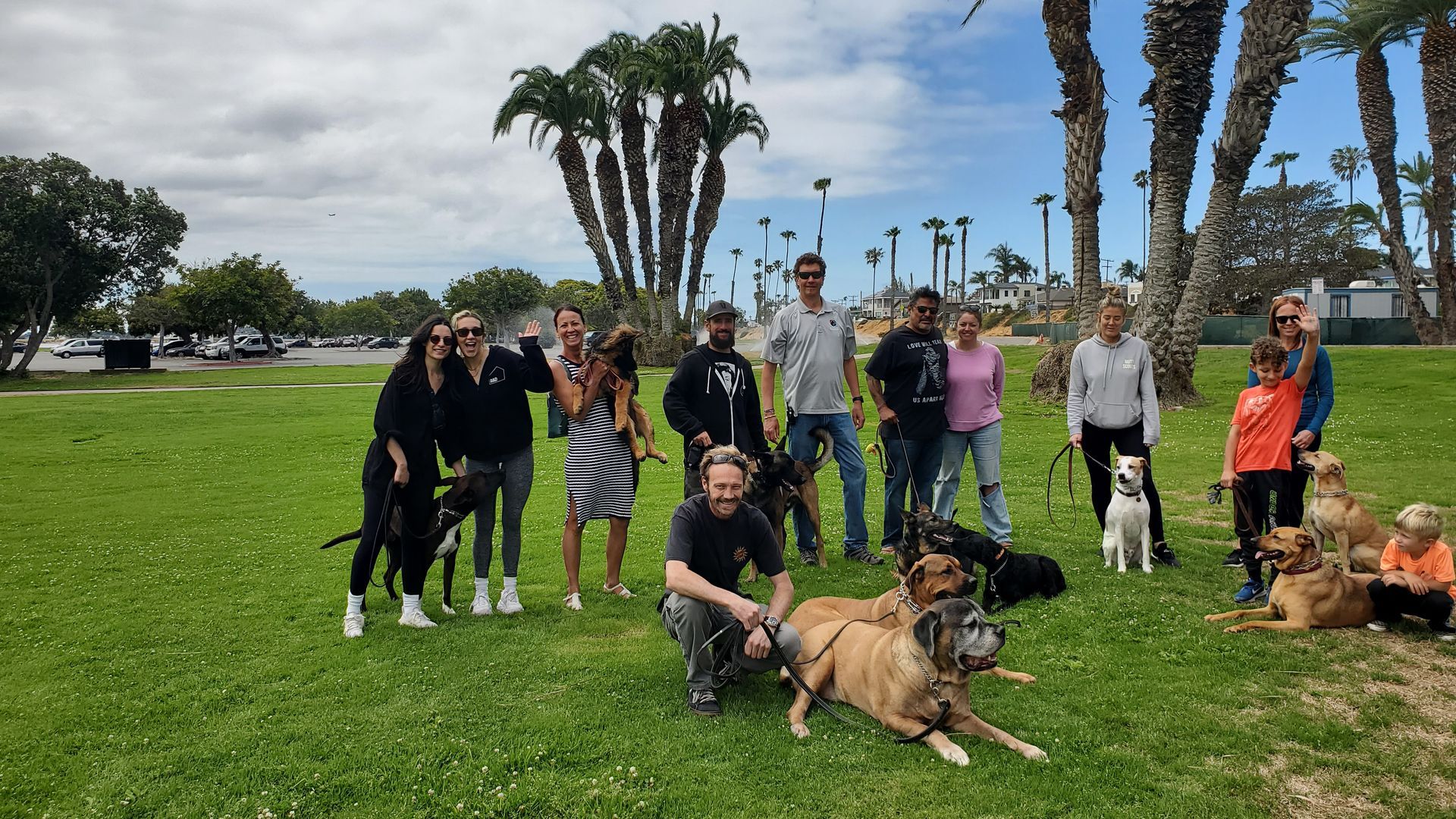A group of people are posing for a picture with their dogs in a park.